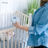 Mother holding the Ameda Mya Joy PLUS breast pump beside a cot