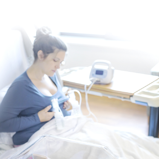 Mother expressing with the Ameda Pearl breast pump in a hospital room, collection bottles on the bedside table
