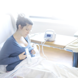 Mother expressing with the Ameda Pearl breast pump in a hospital room, collection bottles on the bedside table