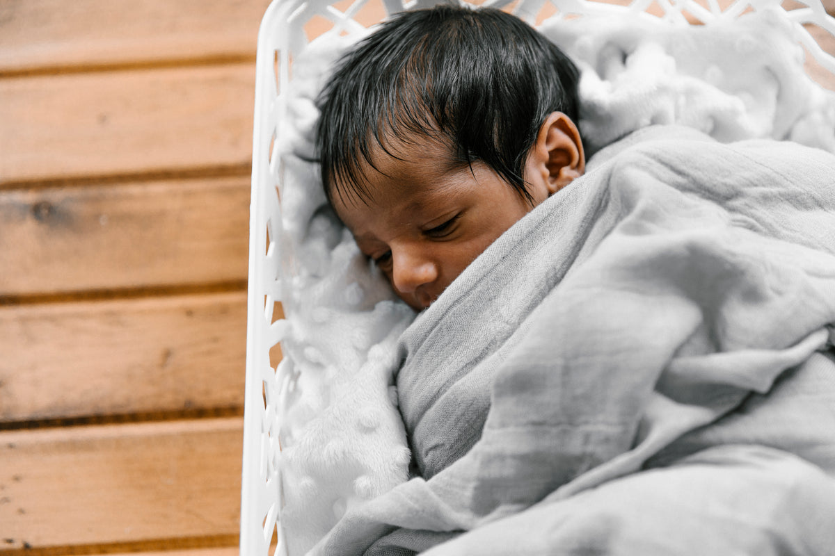 A sleeping newborn wrapped in a soft grey blanket in a white bassinet