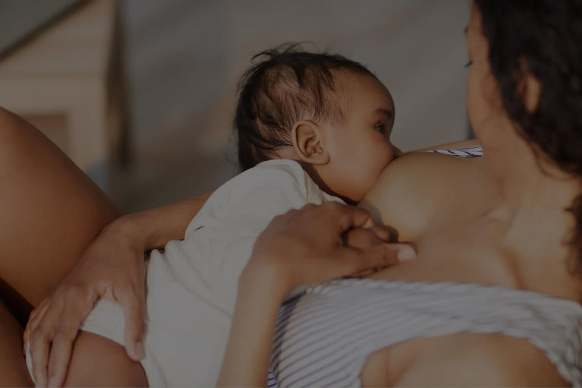 A mother breastfeeding her baby at home, warmly lit